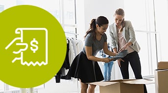 Two women unpack or sort clothes in an office or store setting with racks of clothing in the background. A large green circle with a white icon of a hand holding a receipt with a dollar sign is on the left side of the image.