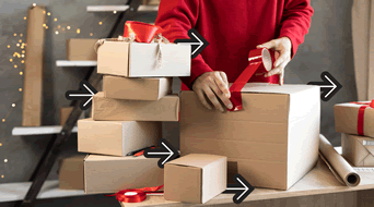 A person in a red sweater is wrapping a large cardboard box with red ribbon on a table. Several other wrapped boxes and ribbons are stacked nearby. Black arrows point towards the boxes, and fairy lights are in the background.