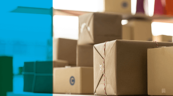 Why 3PL for Small Package-Promo A pile of variously sized cardboard packages stacked on a surface, ready for small business shipping. The left side of the image features a blue overlay. The blurred background hints at an indoor setting, possibly a bustling warehouse or office environment.