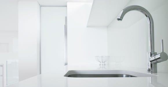 A modern, minimalist kitchen with a sleek chrome faucet, white countertop, and sink. The clean white interior features two glass bowls—perfect for specialty shipping or displaying fragile shipping essentials in style.