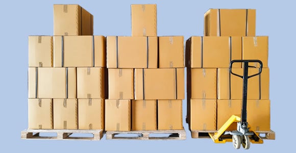 Several stacks of cardboard boxes, marked for specialty shipping, are arranged on wooden pallets with a yellow hand pallet jack in front of one stack, all set against a light blue background.