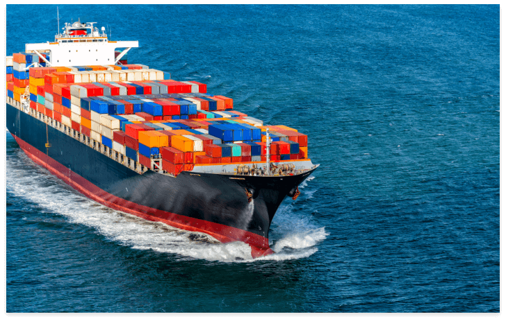A large cargo ship loaded with stacks of colorful shipping containers sails through the blue ocean, reminding businesses and shoppers of approaching holiday shipping deadlines as it creates white waves at the bow.