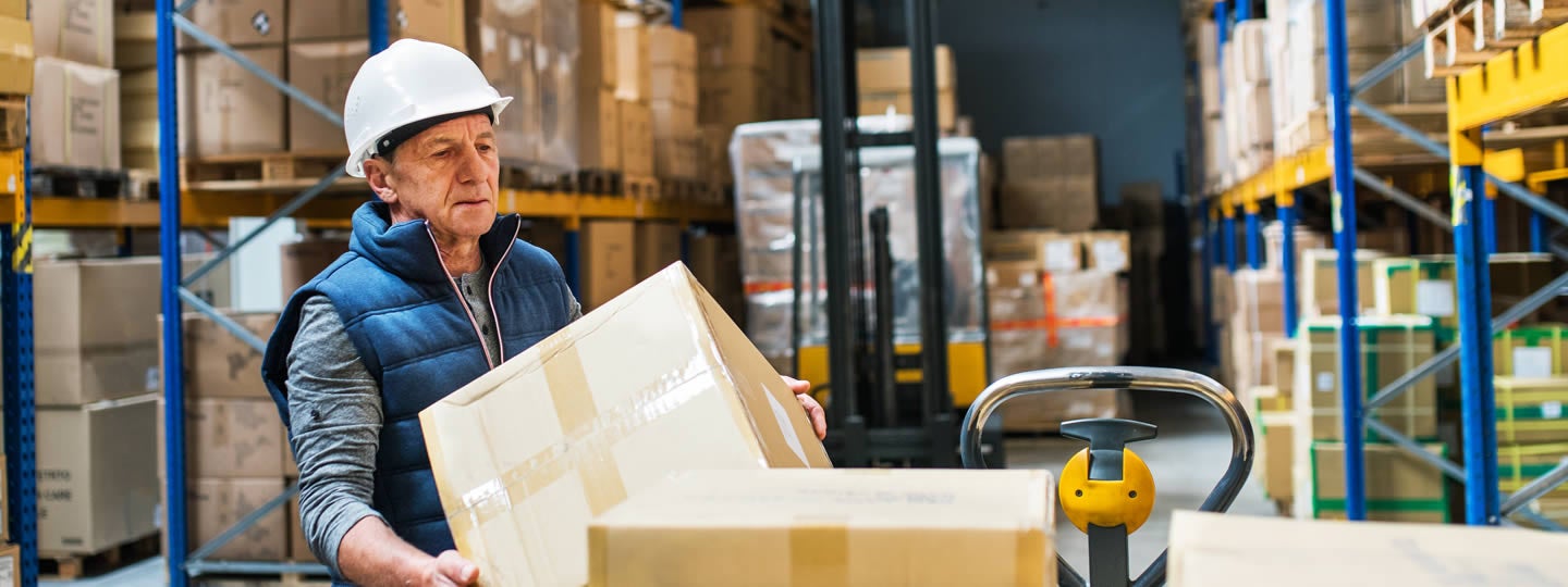 while a woman with red hair opens one on a table. Both are surrounded by stacks of boxes