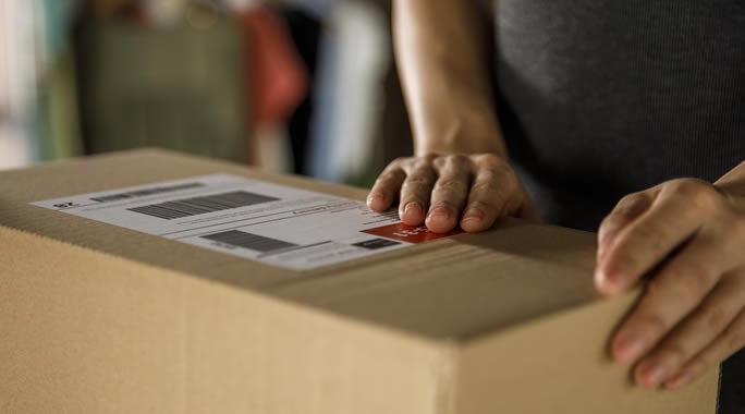 A person holding two stacked cardboard boxes represents a bustling small-business-shipping-hub. On the right
