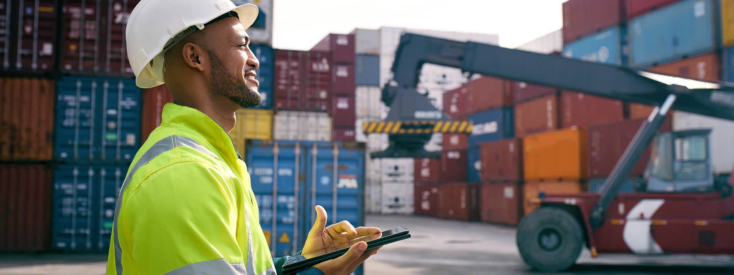 symbolizing movement or progress in logistics.|A person in a high-visibility jacket uses a tablet at a shipping yard