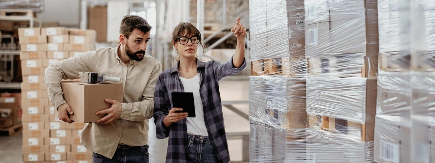 while a man carries a cardboard box nearby. Both are in a warehouse. Colorful arrows are overlaid on the image