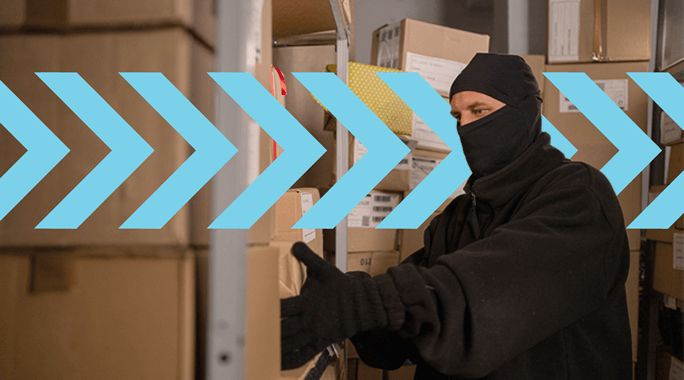 A masked person in dark clothing is handling packages in a storage area filled with cardboard boxes, highlighting the precision of Specialty Freight. Blue chevron graphics overlay the image, pointing to the right.