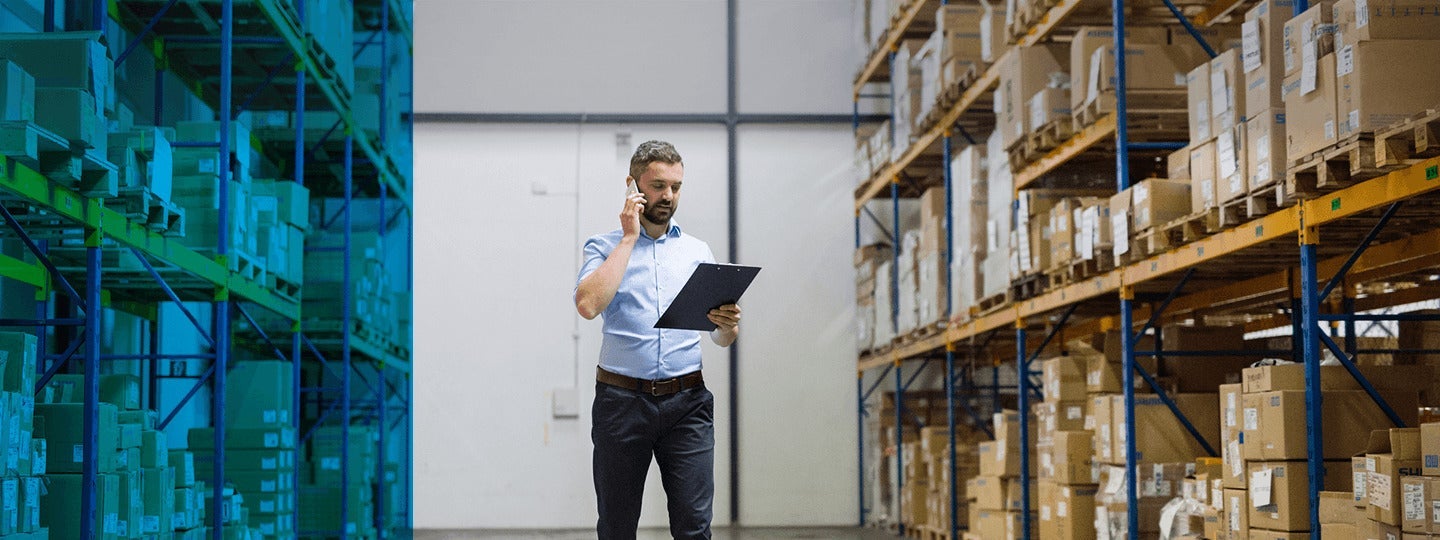 talking on a phone and holding a clipboard. He is surrounded by shelves stacked with boxes and packages. The lighting is bright