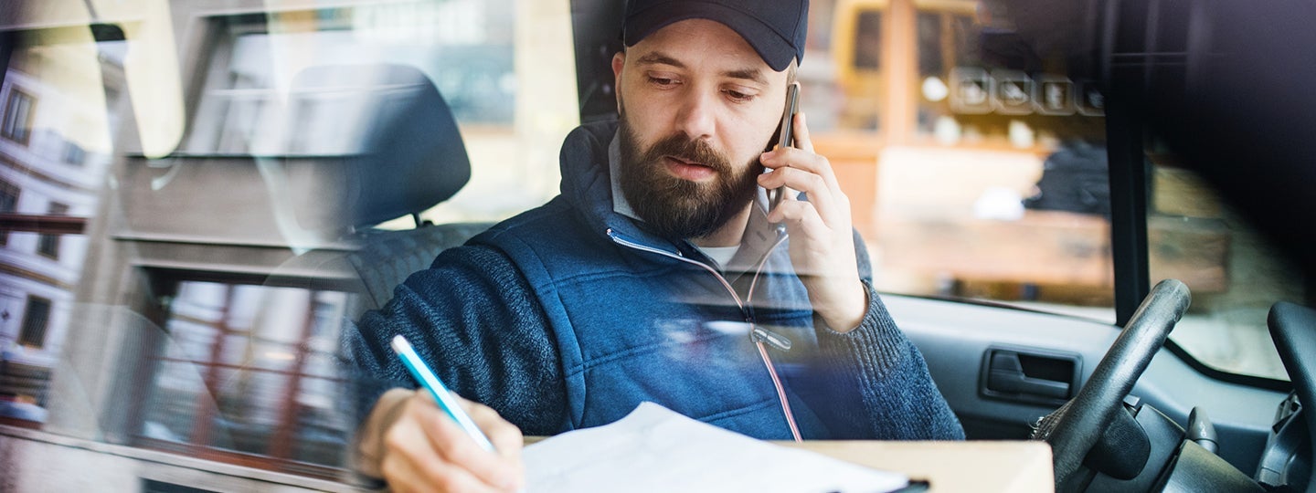 talking on a cellphone. He is writing on a notepad with a pen. The focus is on his focused expression