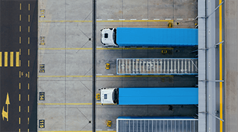 Aerial view of three blue trucks parked parallel in designated spaces at a small-business-shipping-hubs loading dock. Yellow lines and numbers neatly mark the parking spots on the concrete surface.|Aerial view of two blue trucks