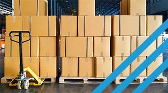 Stacks of brown cardboard boxes on wooden pallets in a warehouse. A yellow hand pallet truck is positioned in front of the boxes. Blue diagonal lines are overlaid on the right side of the image.|A stack of cardboard boxes rests on wooden pallets in a warehouse