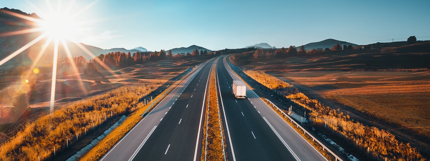 and there are white and an orange arrow pointing right above the scene.|A 3PL truck drives down a straight