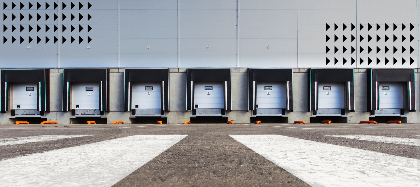 evenly spaced along a gray industrial building. A wide asphalt area with painted white diagonal lines is in the foreground