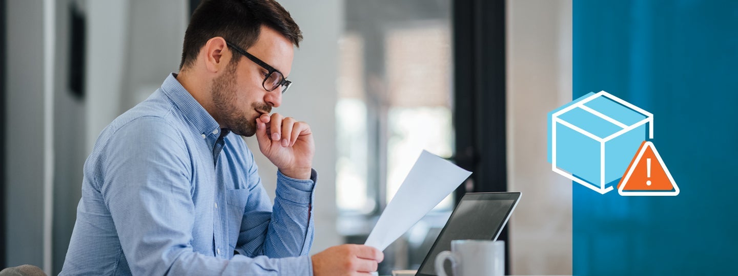 looking at a piece of paper. A laptop and a white coffee mug are on the table. On the right