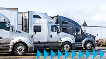 Line of parked semi-trucks in a small-business-shipping-hub under a blue sky. The image shows a side view of the trucks