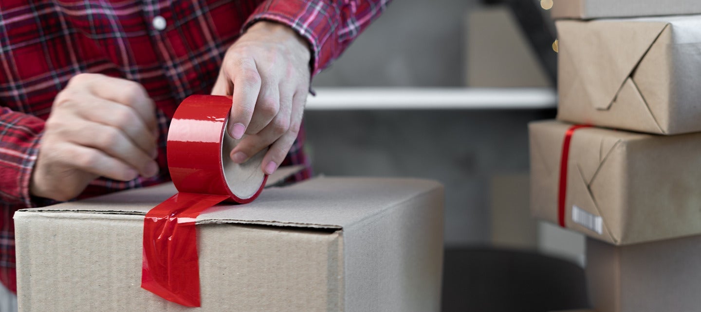 pointing to the right.|A person in a red plaid shirt is sealing a cardboard box with red tape. Nearby