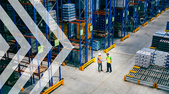 Two workers in safety gear stand in a large warehouse aisle