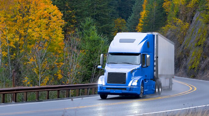 A blue semi-truck navigates a wet