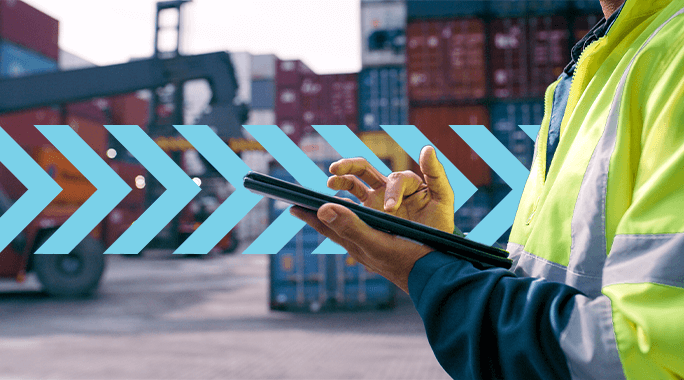 A person in a high-visibility jacket uses a tablet at a busy shipping container yard. Blue arrows are overlaid on the image