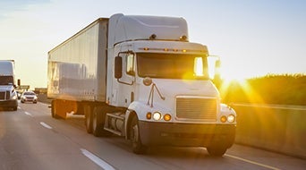 A white semi-truck with a trailer drives on a highway at sunset