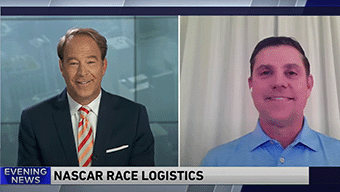 A news broadcast shows two men on a split screen discussing NASCAR race logistics. The left side features a suit-clad man labeled Evening News