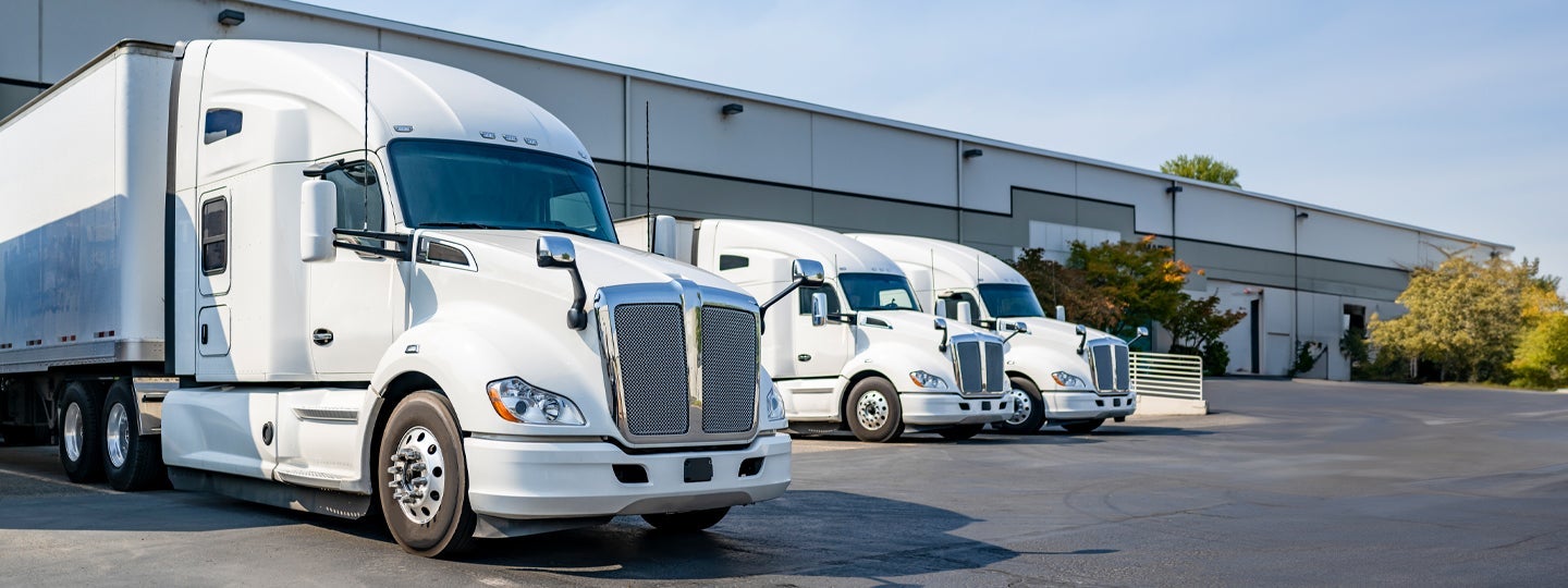 suggesting motion or progress. The sky is clear and sunny.|Three white semi-trucks
