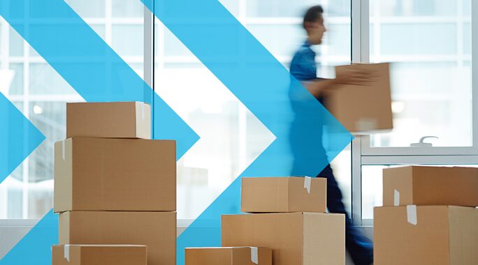 A person carrying a box walks past several stacked cardboard boxes. The background features large windows with a blue arrow graphic overlayed