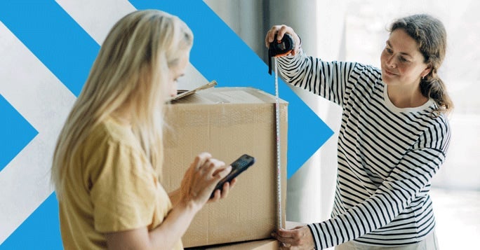 Two women work together with a cardboard box; one measures it with a tape measure while the other checks Shipping AI on her smartphone. A blue arrow pattern is in the background.