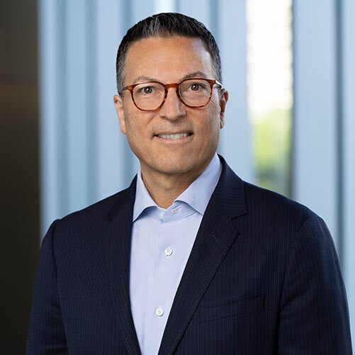 Jack Pearlstein, wearing glasses, a dark suit, and a light blue dress shirt, smiles at the camera. The background features vertical, blurred blue and white lines with a subtle xModal touch.