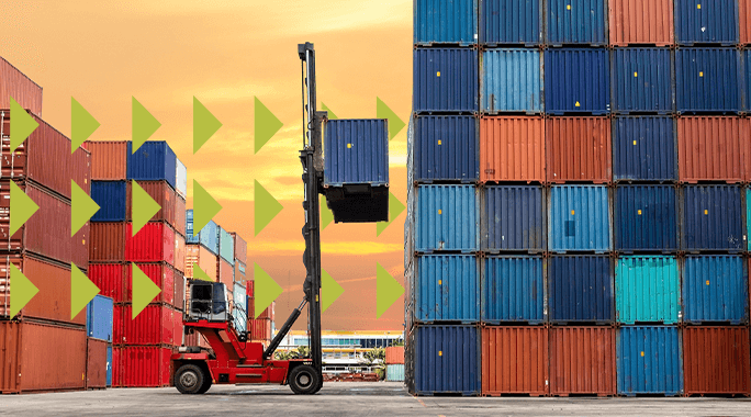 A forklift lifts a shipping container between tall stacks of colorful containers at a shipping yard during sunset, with green arrow graphics overlayed on the left side—highlighting potential accessorial charges in logistics operations.