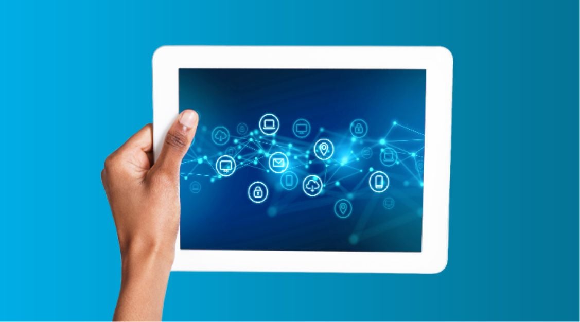 A hand holds a white tablet displaying digital network icons connected by lines on a blue background, symbolizing connectivity, technology, and the power of a supply chain control tower.