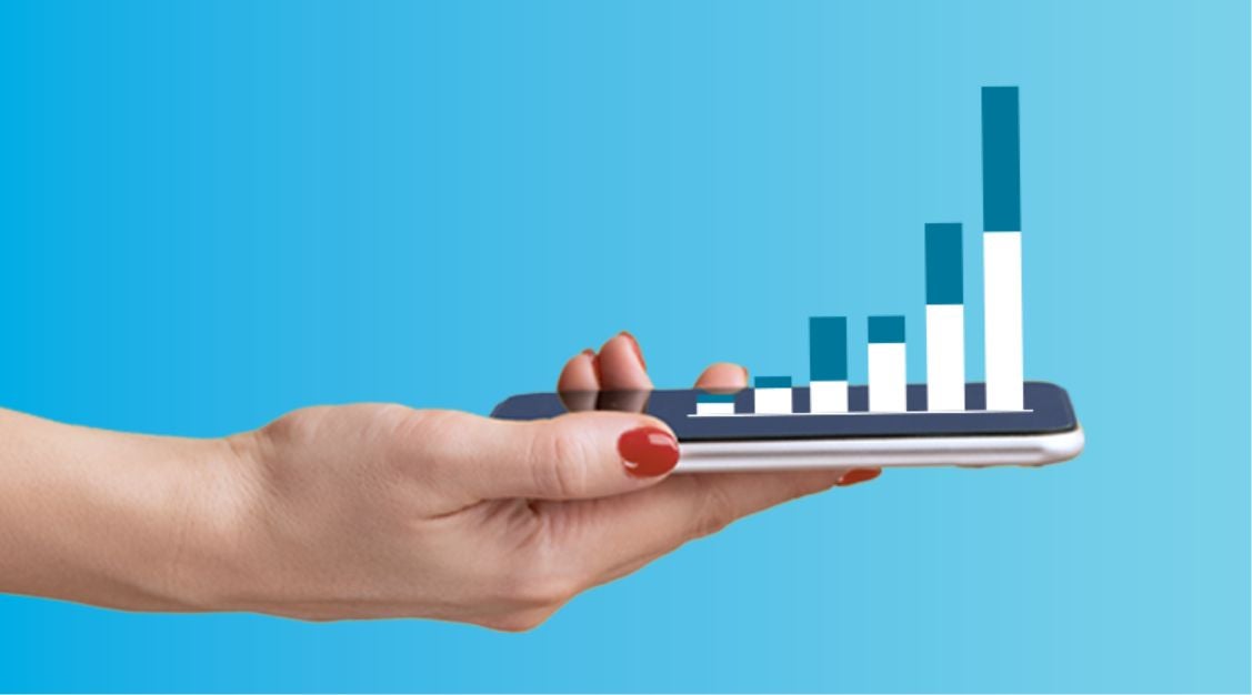 A hand with red nail polish holds a smartphone displaying a 3D bar graph with rising columns, symbolizing growth or data analysis empowered by a supply chain control tower, set against a blue gradient background.