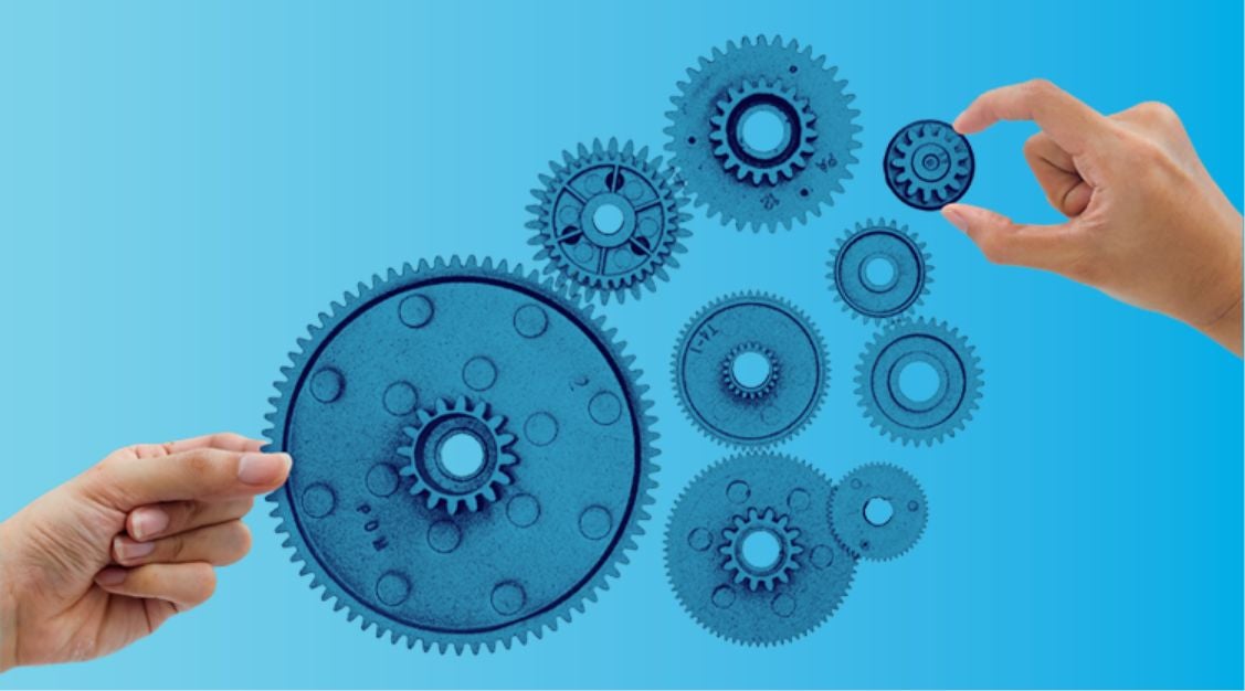 Two hands are holding blue gears against a gradient blue background, with several interlocking gears in the center, symbolizing teamwork and the coordination seen in a supply chain control tower.