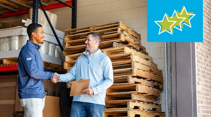 Two men shake hands in a warehouse, with wooden pallets stacked behind them. One holds a clipboard. A blue square with three green stars is displayed in the upper right corner.