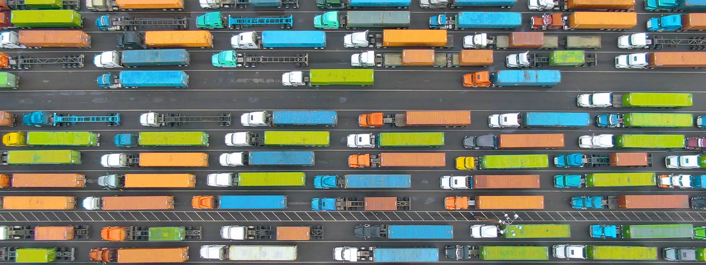 Aerial view of multiple rows of colorful trucks, possibly transporting goods with a Hazmat Bill of Lading, parked in parallel lines in a lot, featuring trucks in bright shades like blue, orange, yellow, and green.