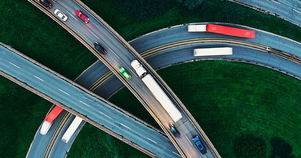 Aerial view of highways and overpasses with cars and trucks traveling in different directions, surrounded by green grass—an essential network that helps ship large items efficiently across regions.