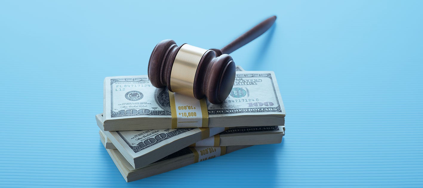 A judge’s gavel rests on top of three stacks of one hundred dollar bills, symbolizing the intersection of law and money—such as cases involving tariff refund disputes—on a light blue background.
