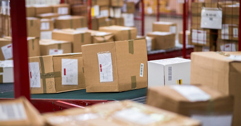 Cardboard packages on a moving conveyor belt in a warehouse during freight peak season.